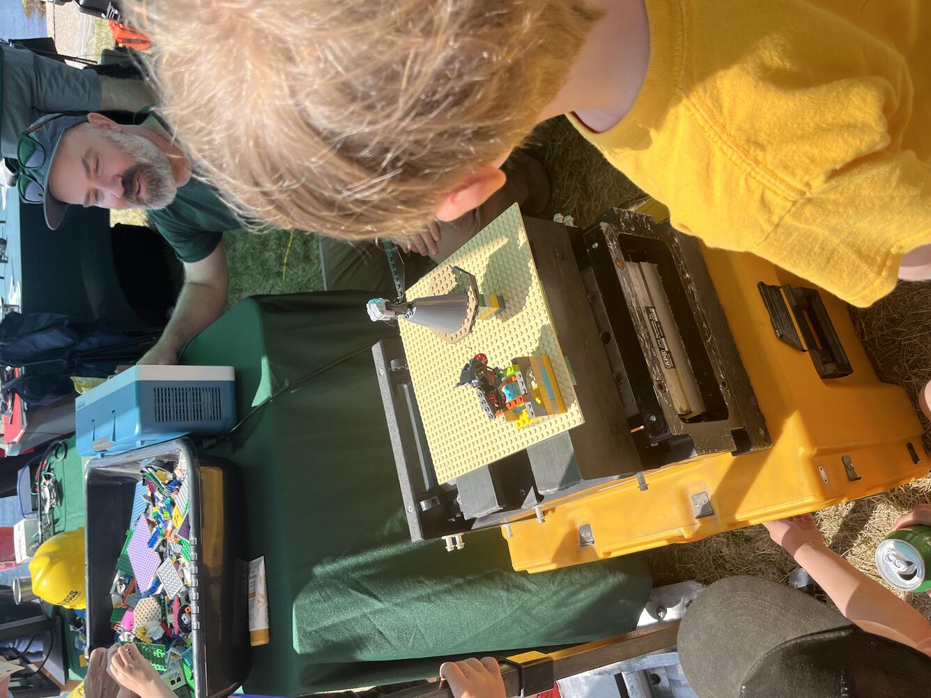shake table with legos on it and kids standing around it and a USGS scientist kneeling near it