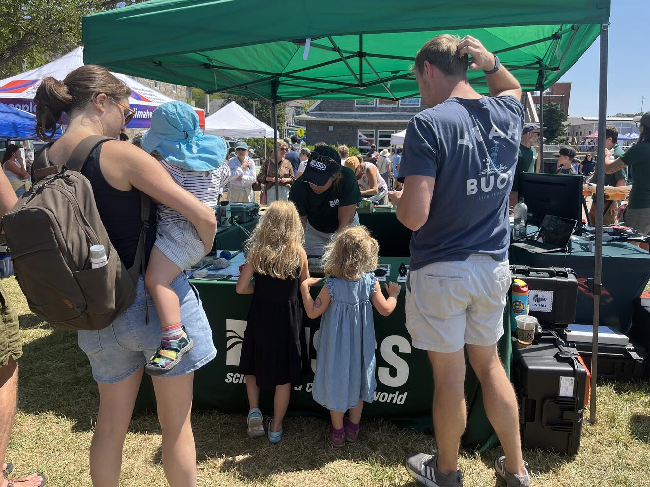 a family with three kids visiting the USGS booth outside under a green tent