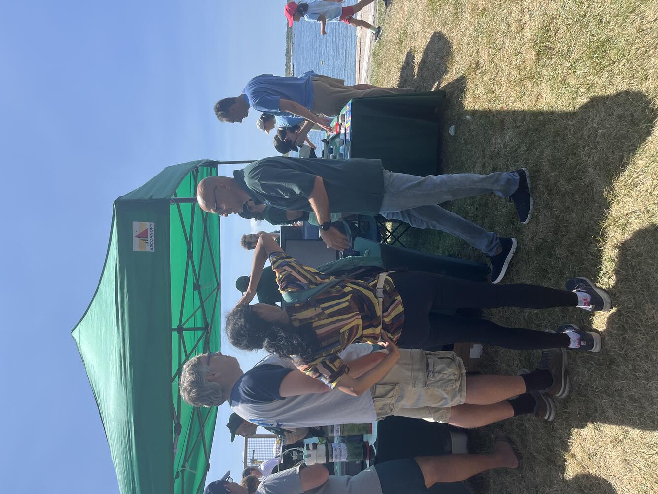 Two people talking to USGS scientist next to USGS booth outside under green tent on a sunny day