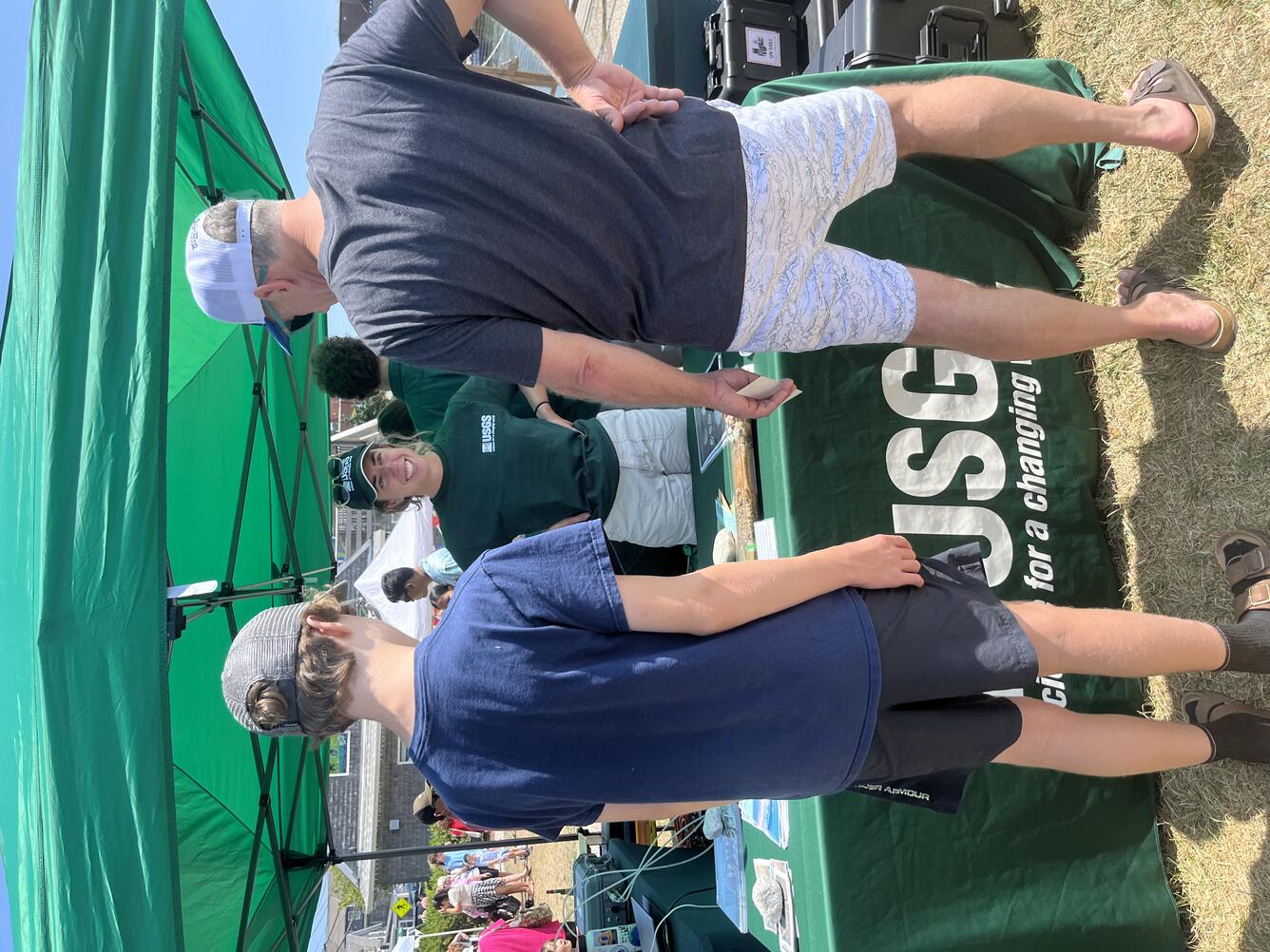 woman smiling, talking to a man and kid, outside at USGS booth