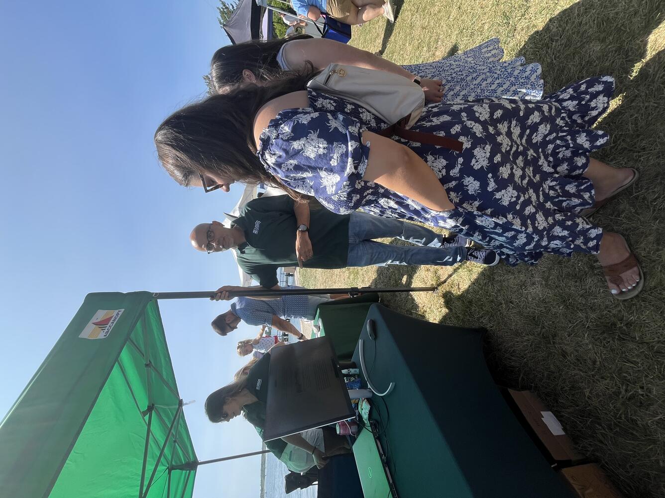 person in USGS shirt standing next to USGS booth and tent, talking to two people referencing a computer monitor