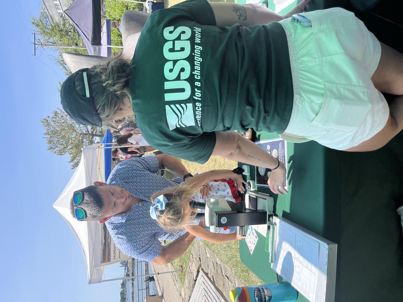 Father holding daughter up to look through microscope, while USGS 