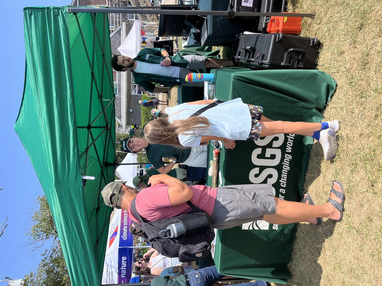 Man and child talking to USGS scientist at booth under tent outside