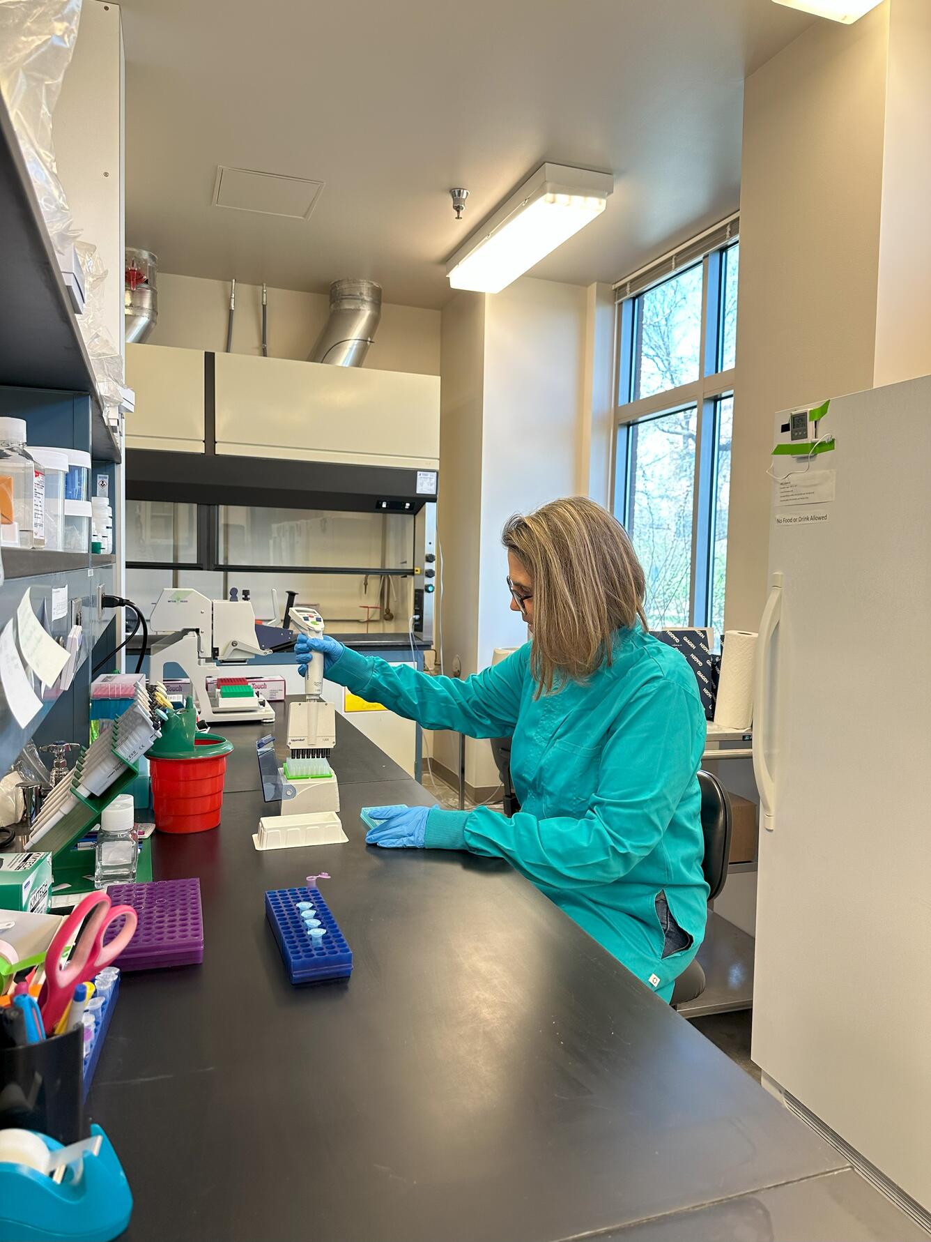 a researcher in a teal lab coat pipettes at a lab bench