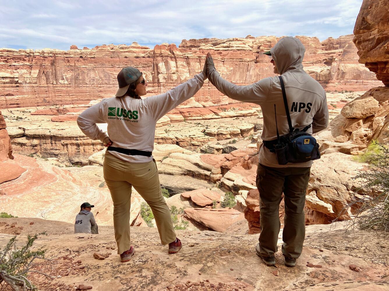 A USGS and NPS scientist give each other a high-five while doing fieldwork