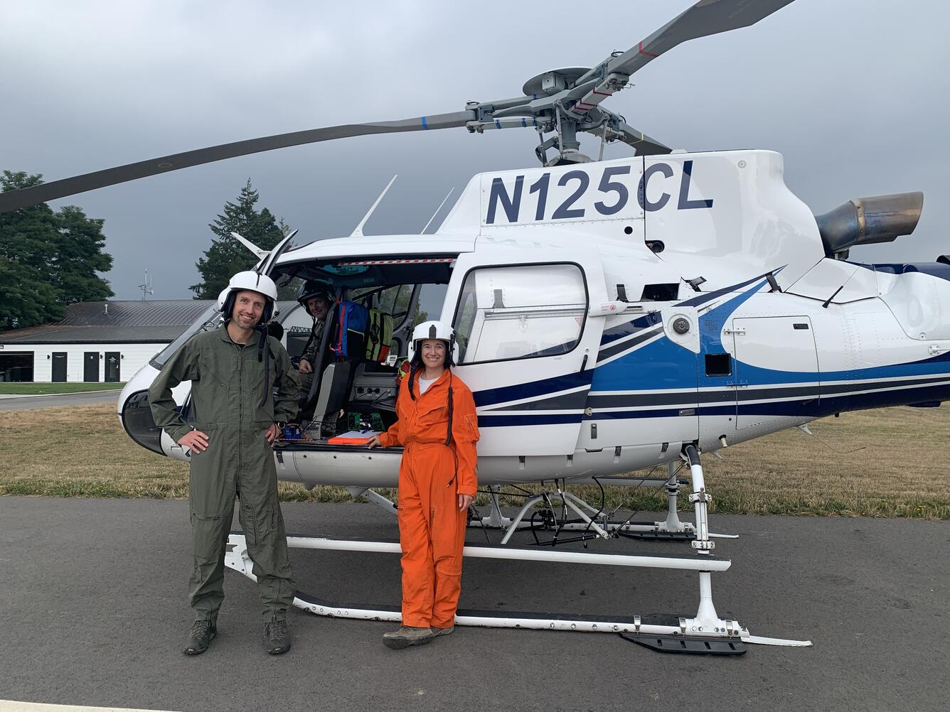 Color photo of two scientists standing in front of a helicopter. 