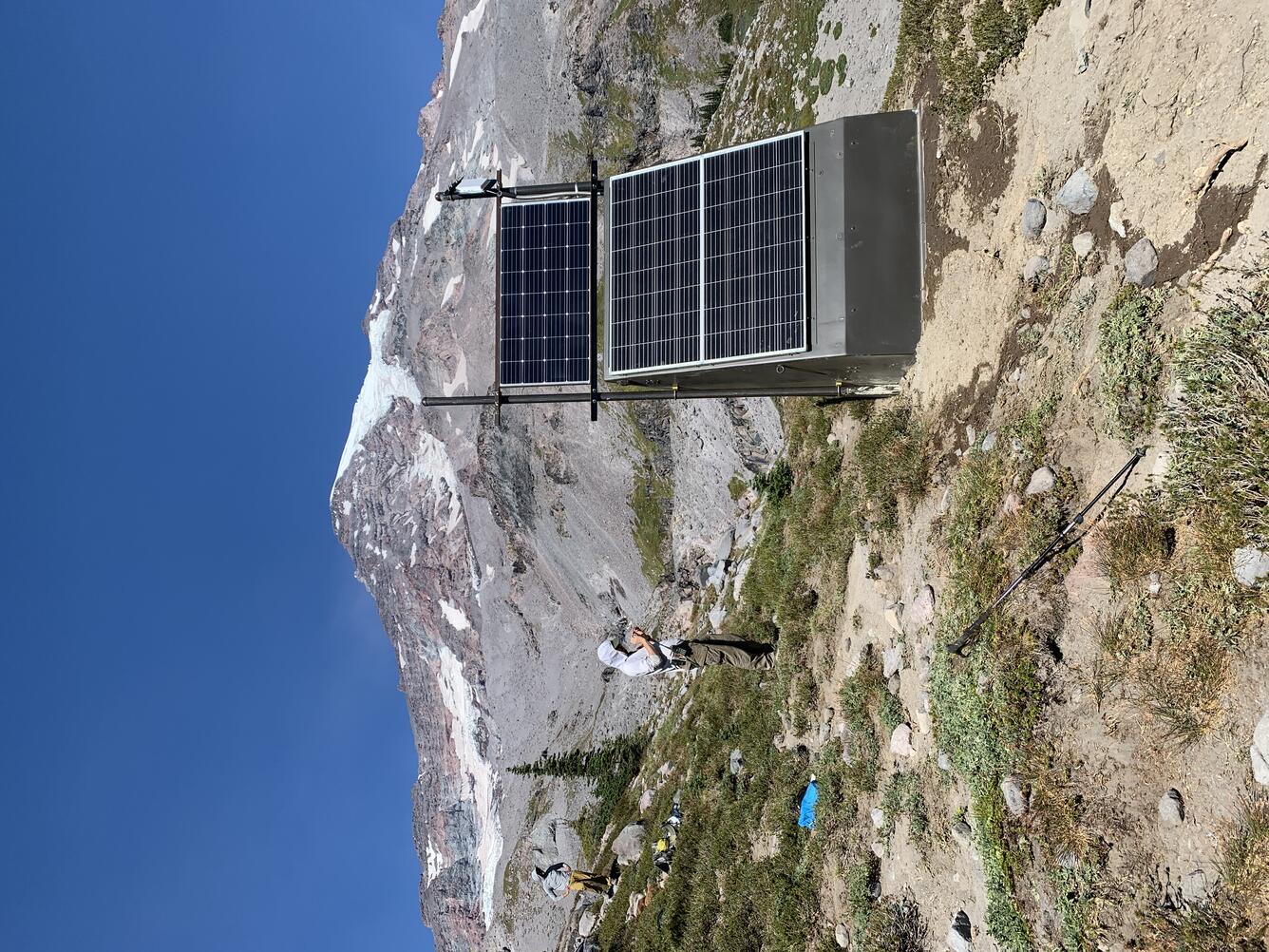 two scientists take field notes beside a volcano monitoring station