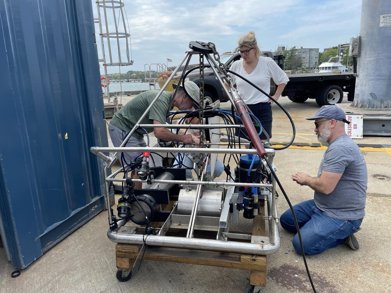 Three people working on a big instrument on a dock