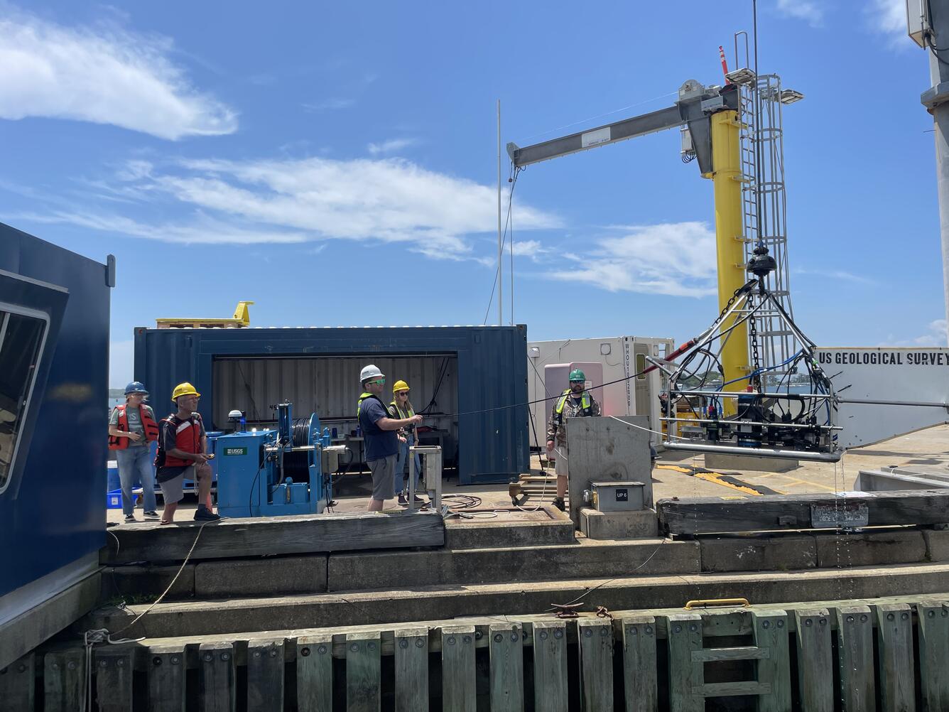 People on dock lowering large piece of equipment into the water