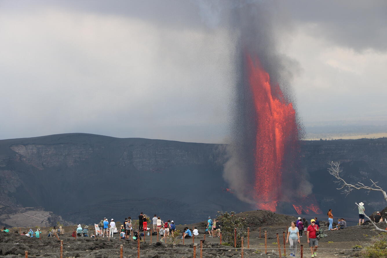 Lava fountains in the background with visitors visible in the foreground