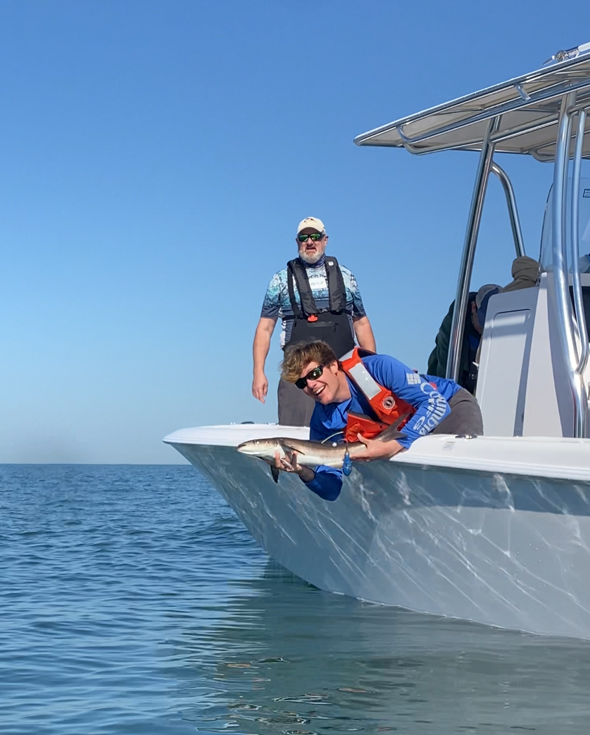 A person releases a fish off a boat while another person watches