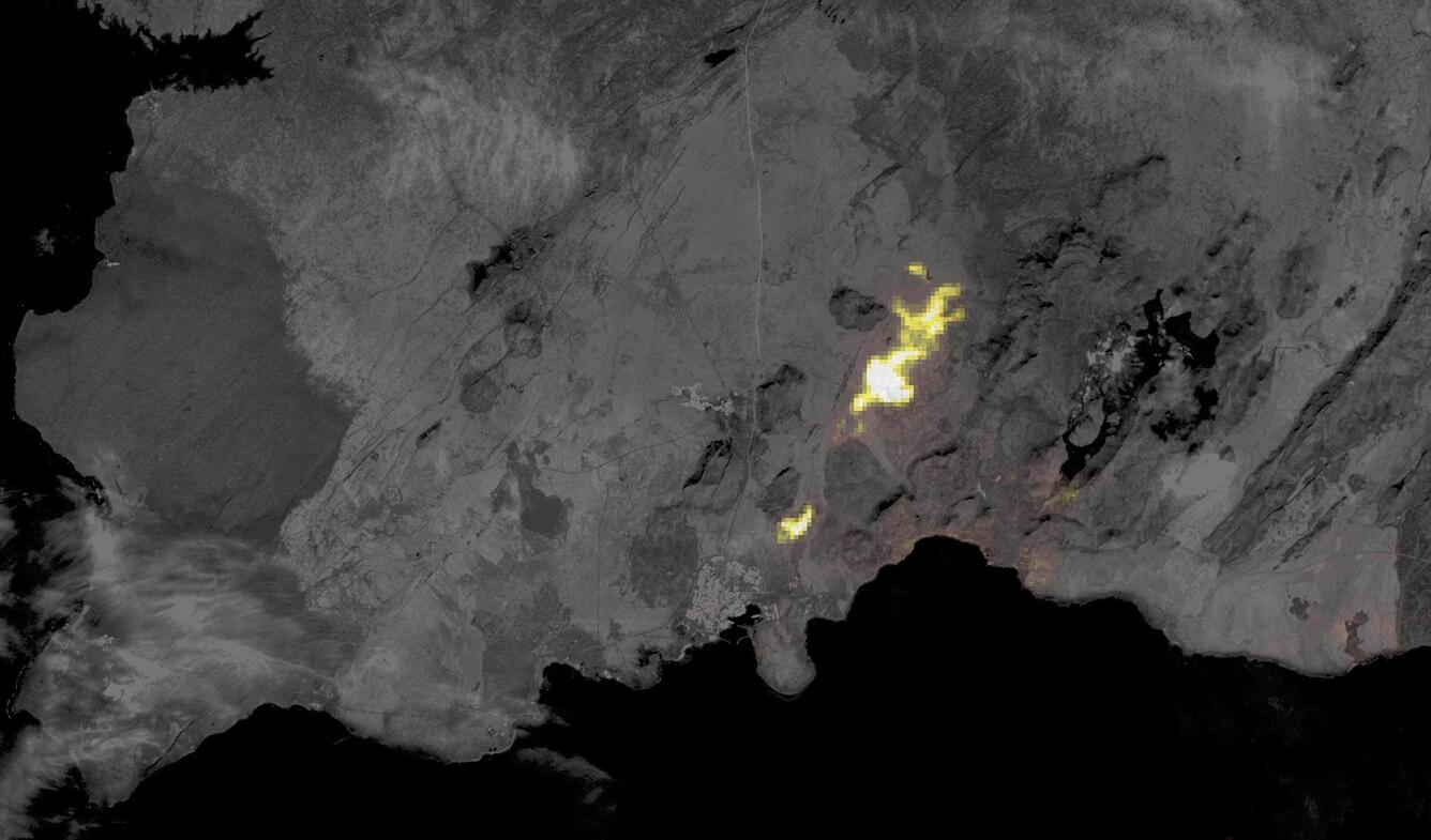 A thermal satellite image of an area of an erupting volcano that shines yellow to white on a gray landscape