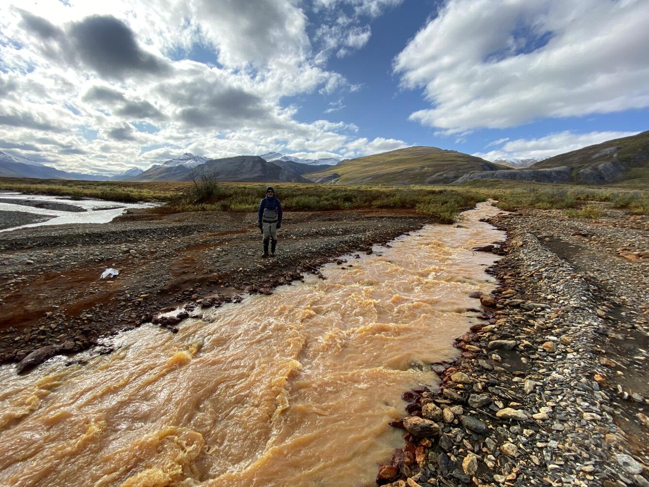 A person standing behind a pale orange river.