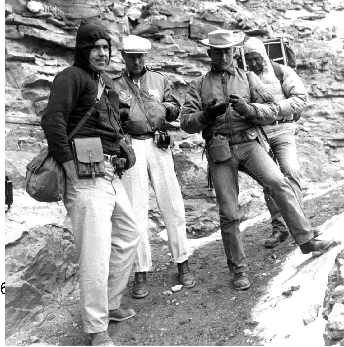 Four men in cold gear standing in front of a rock outcrop