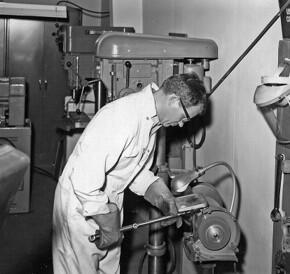 A man in a white jumpsuit works a machine in a machine shop