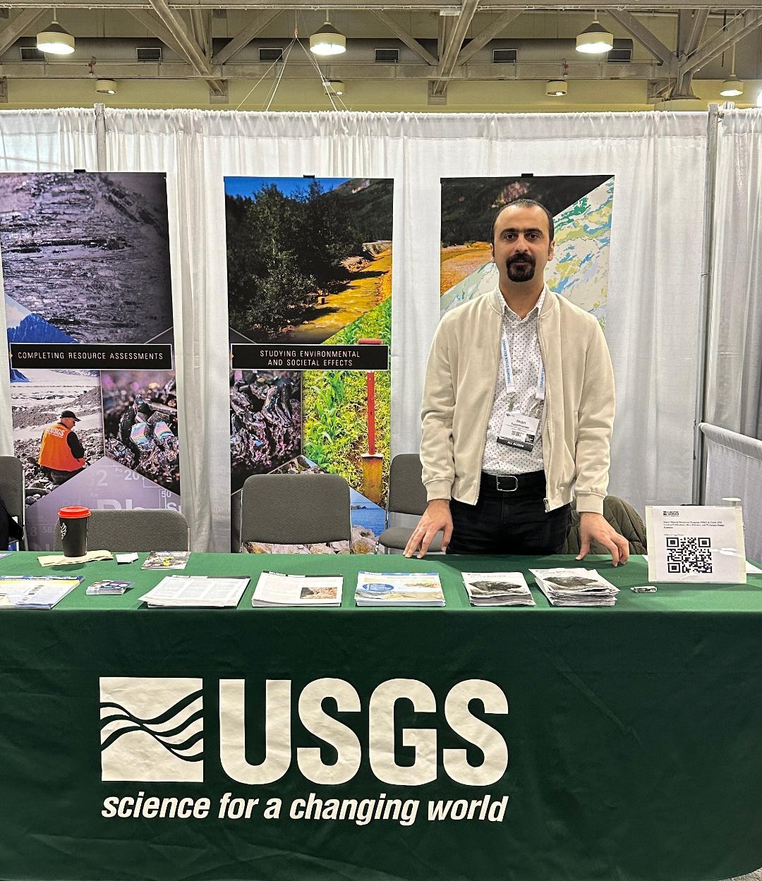 Dr. Iman Salehi Hikouei stands in front of the USGS booth at a conference.