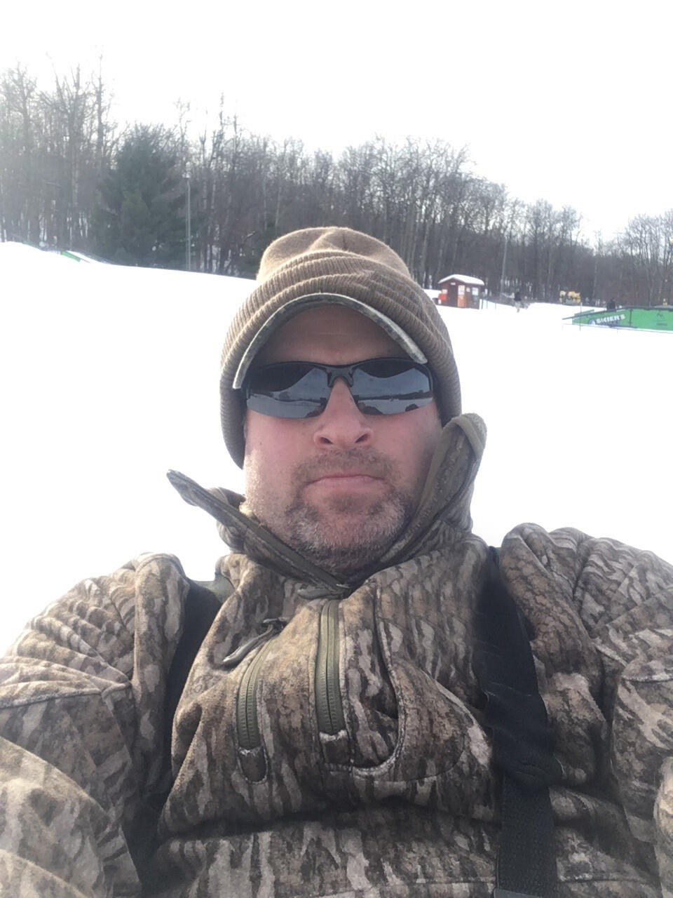 man in the snow wearing a camo jacket, black sunglasses, and a tan hat