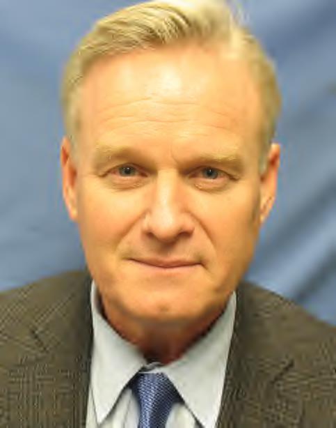 portrait of Jim smiling with blond hair wearing a suit and tie with blue background