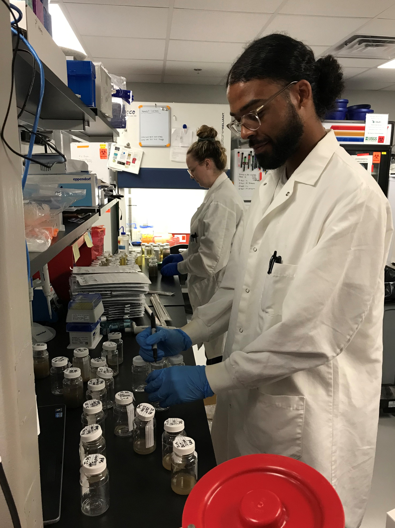 Two scientists in white lab coats preparing samples at a lab bench