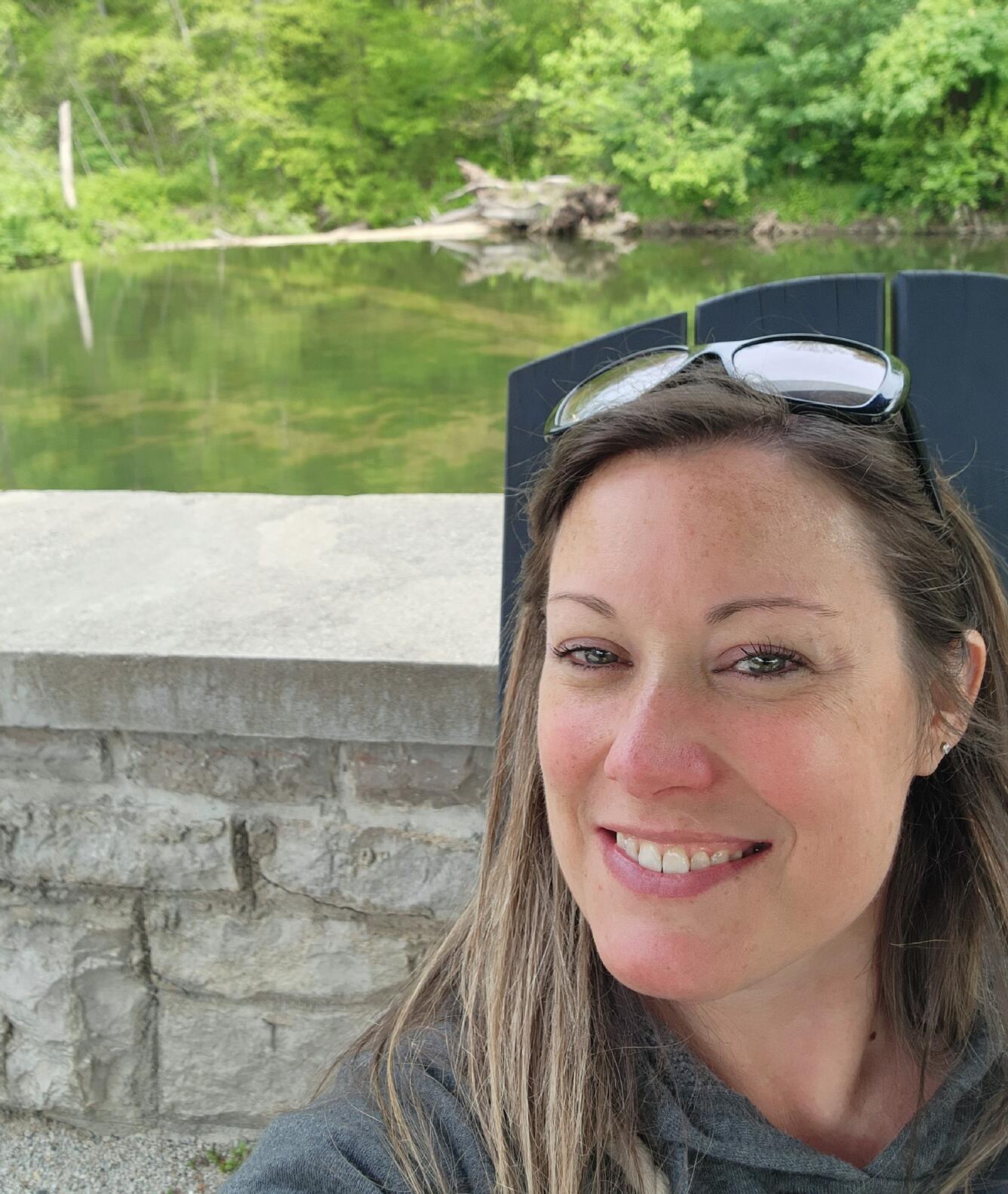 A smiling woman with brown hair standing near and outdoor wall.