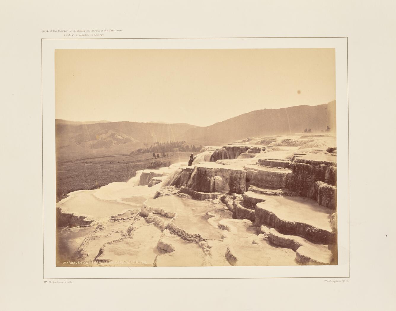 Sepia-toned photo of a man standing on a barren terraced hot spring formation