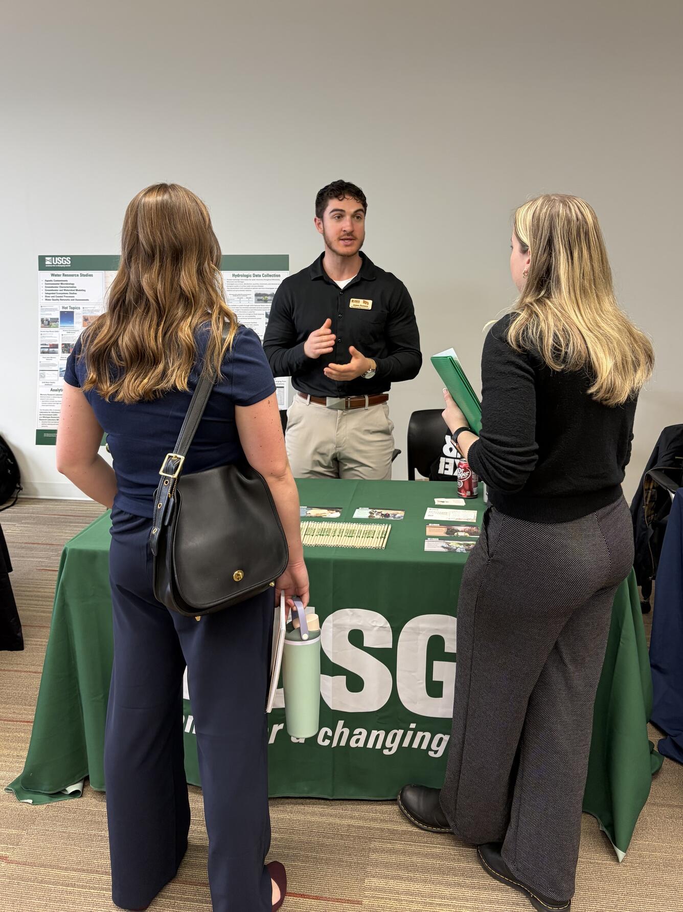 Man standing behind USGS table speaking to two women at a career fair
