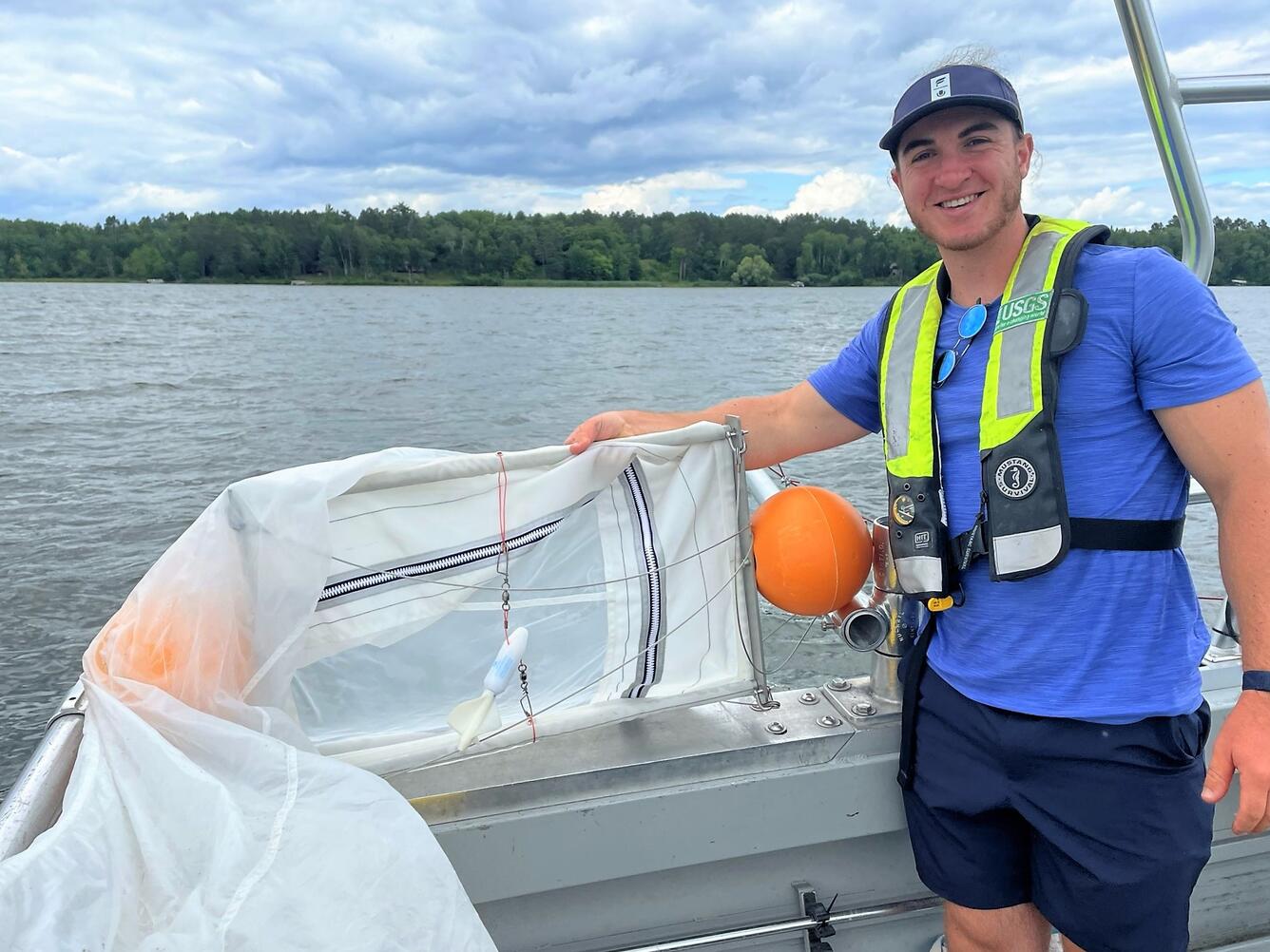 Smiling USGS field scientist on boat holding large microplastics sampling net