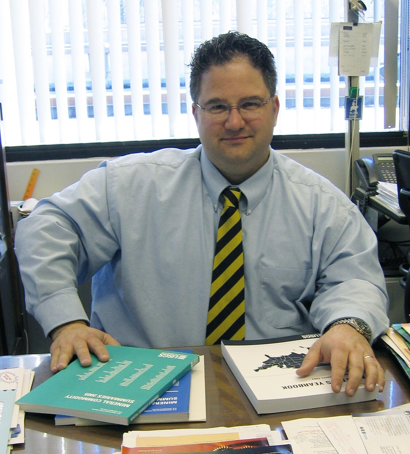 Jason Willett sits at a desk with books on geology on it.