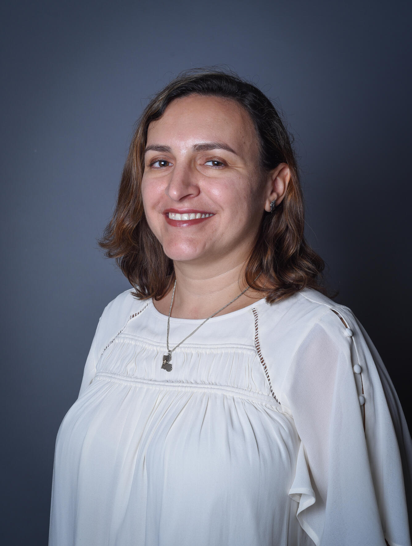 A woman in a white shirt with short brown hair smiles at the camera for her picture.