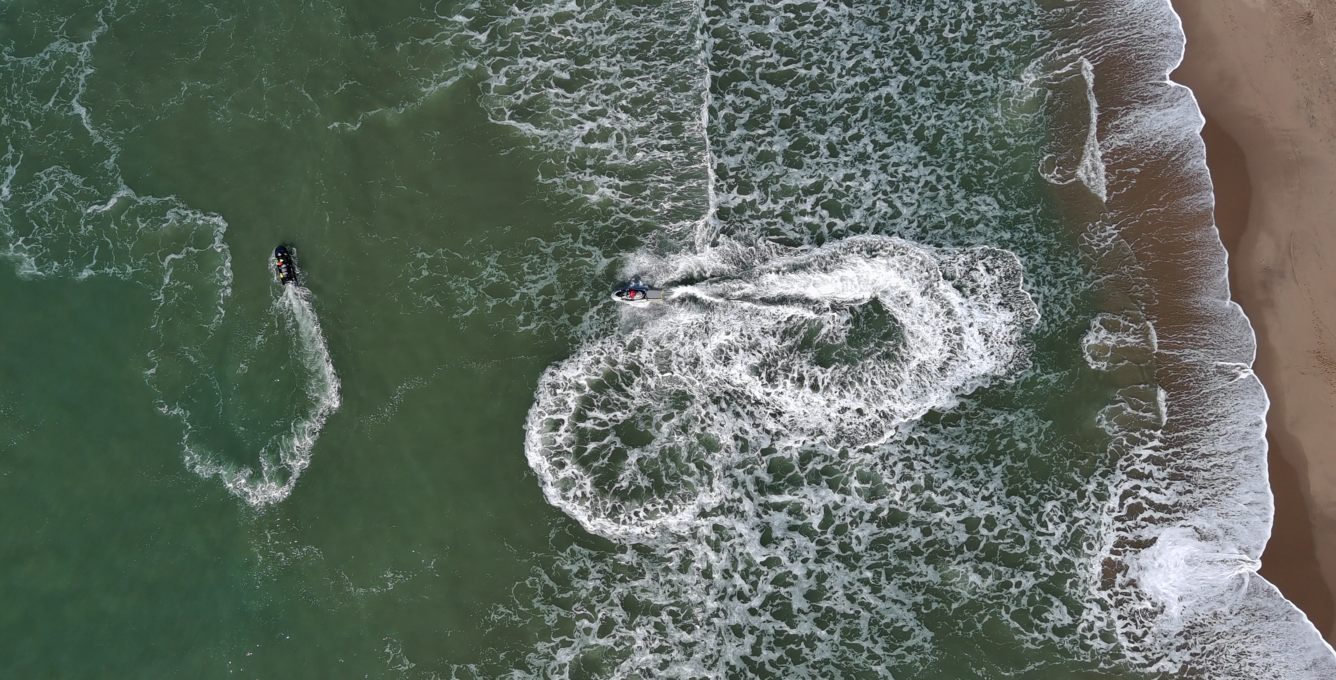 Aerial photo shows researchers operating survey jet skis along a sandy coastline