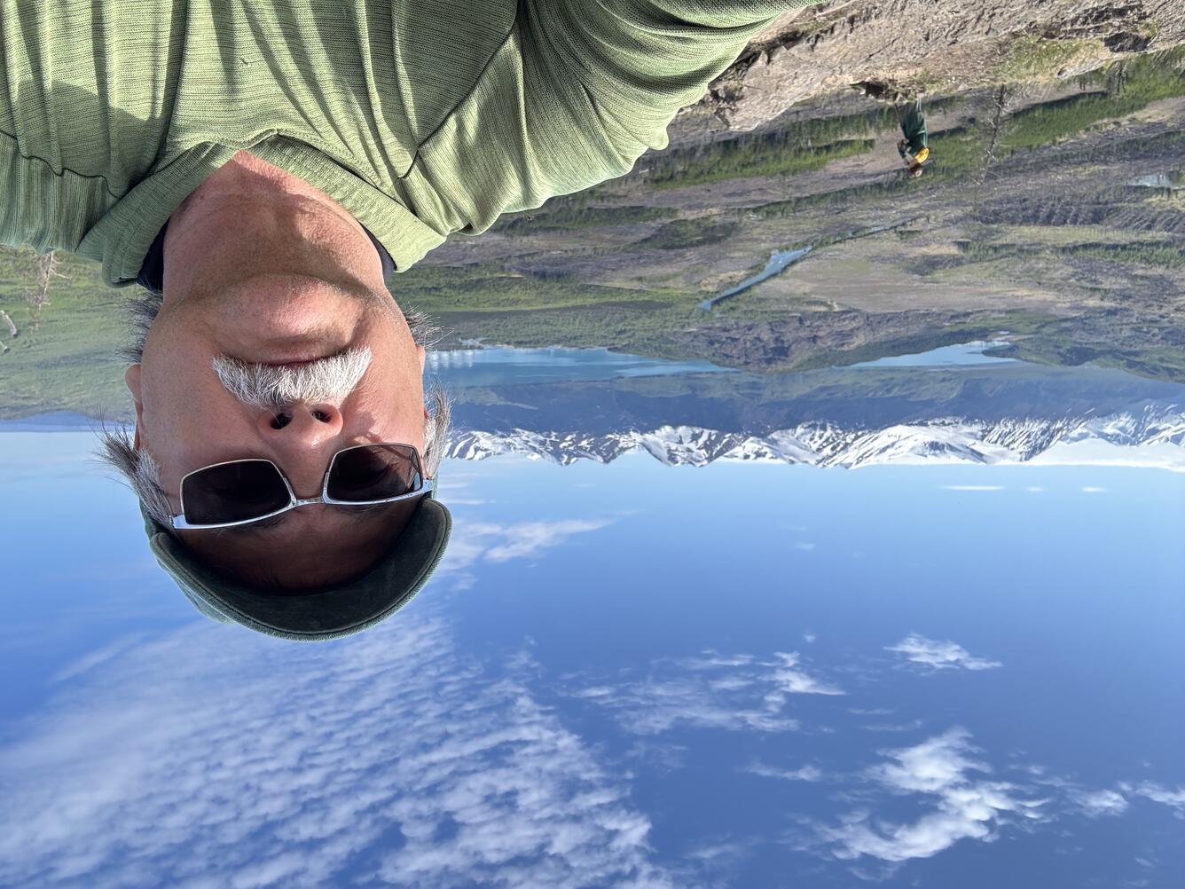 A man takes a selfie with snow-caped mountains in the distance