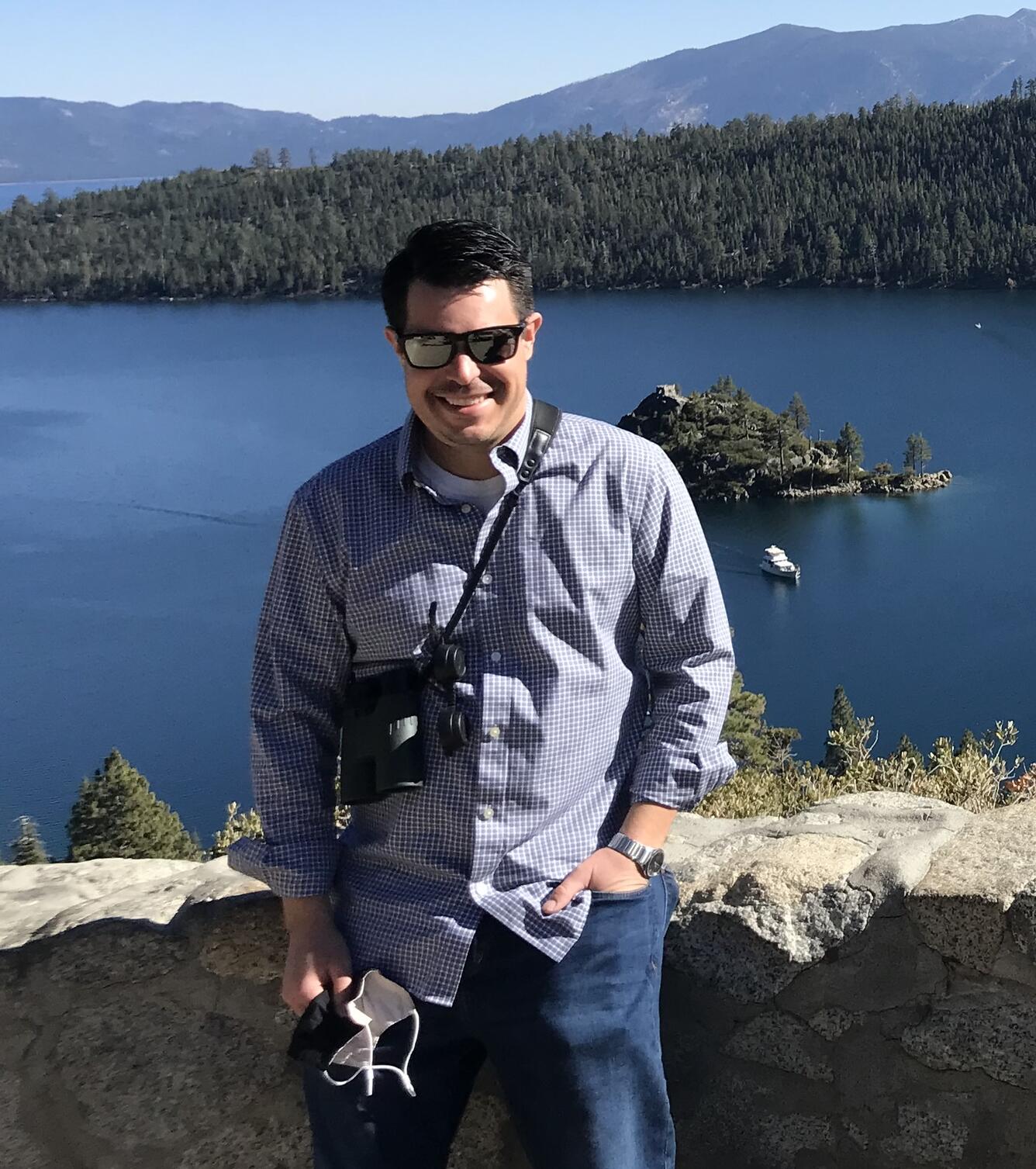 graduate student with dark hair, black glasses, checkered shirt standing near water