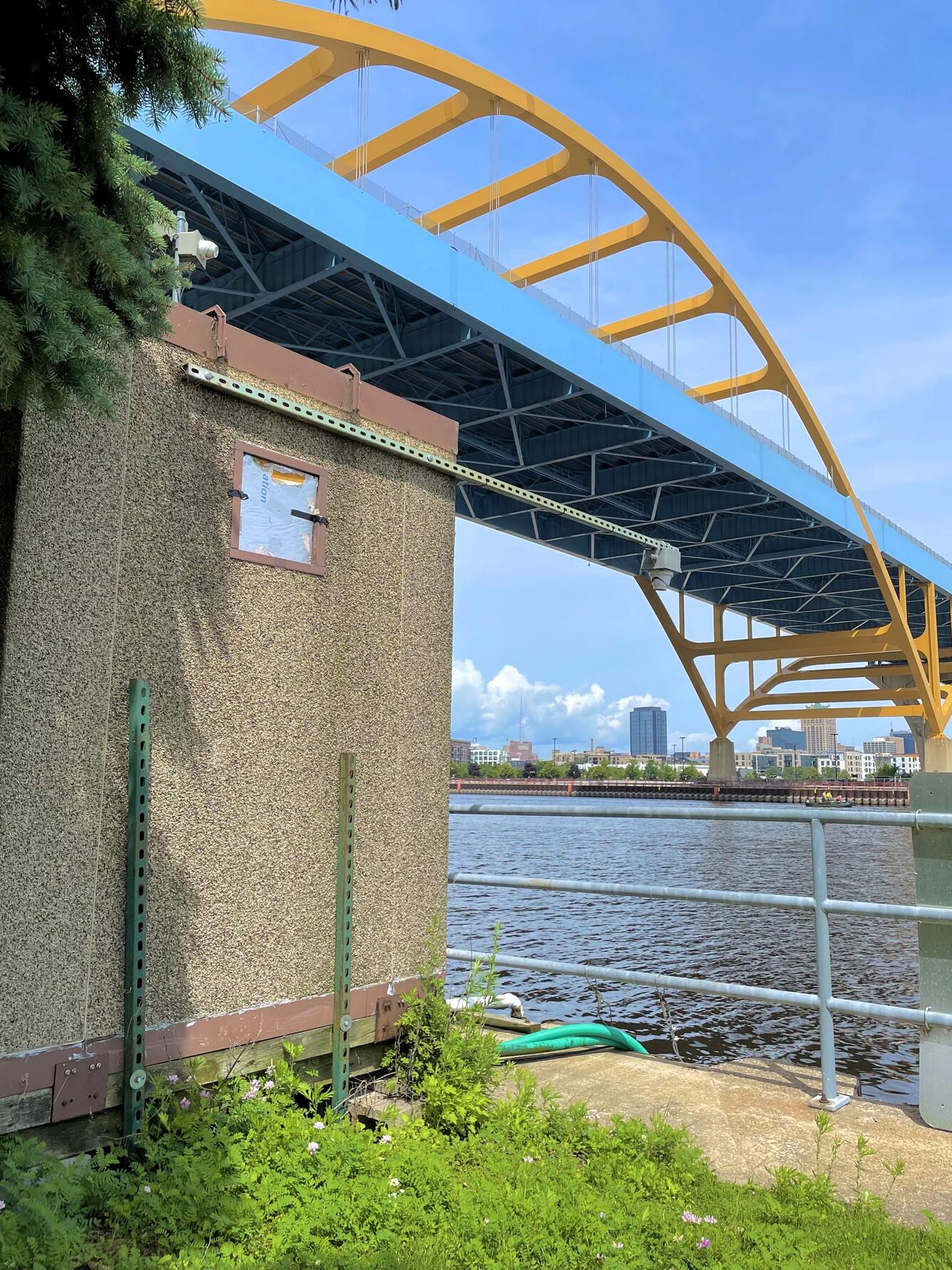 Streamgage housing next to a river with a large suspension bridge in the background