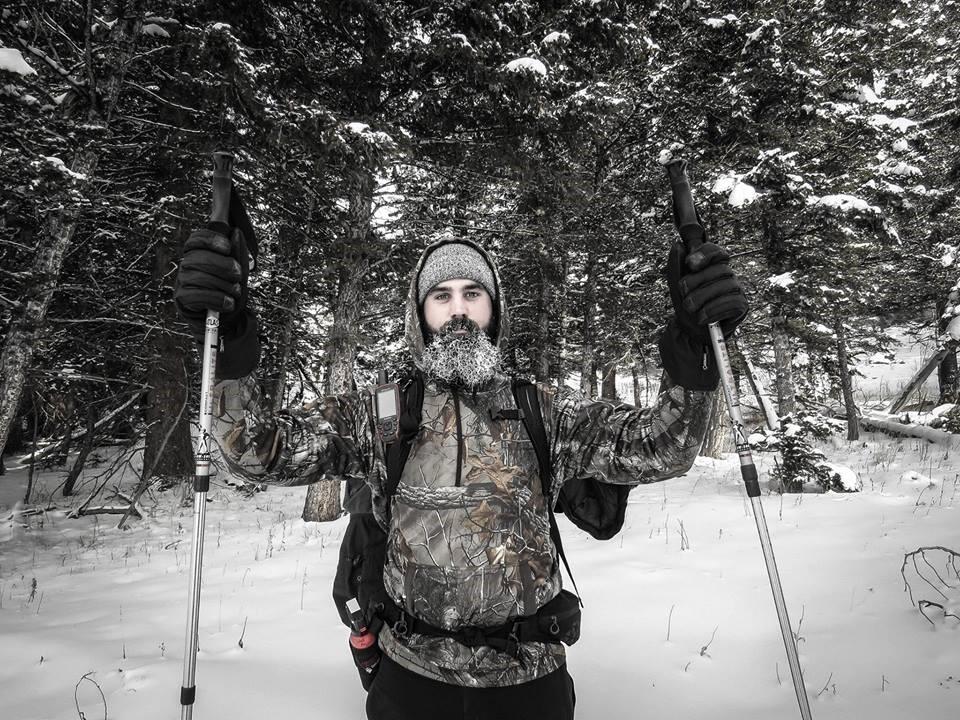 graduate student wearing camo and holding cross country skis in the snow