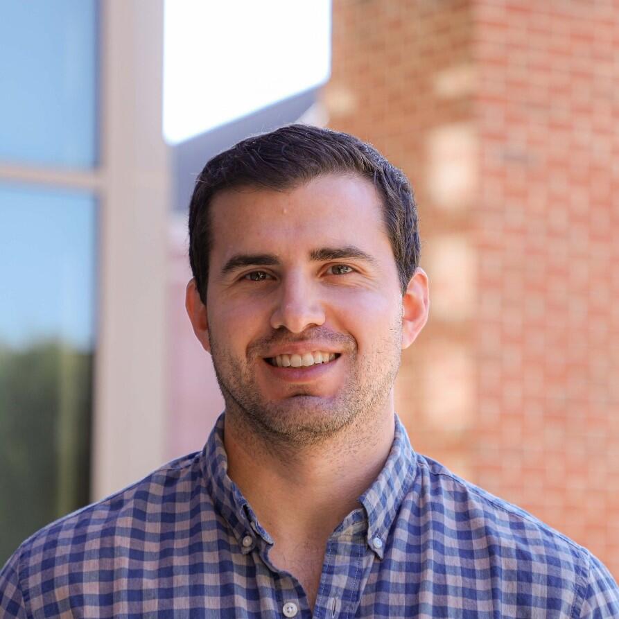 White male dark brown hair in front of brick building 