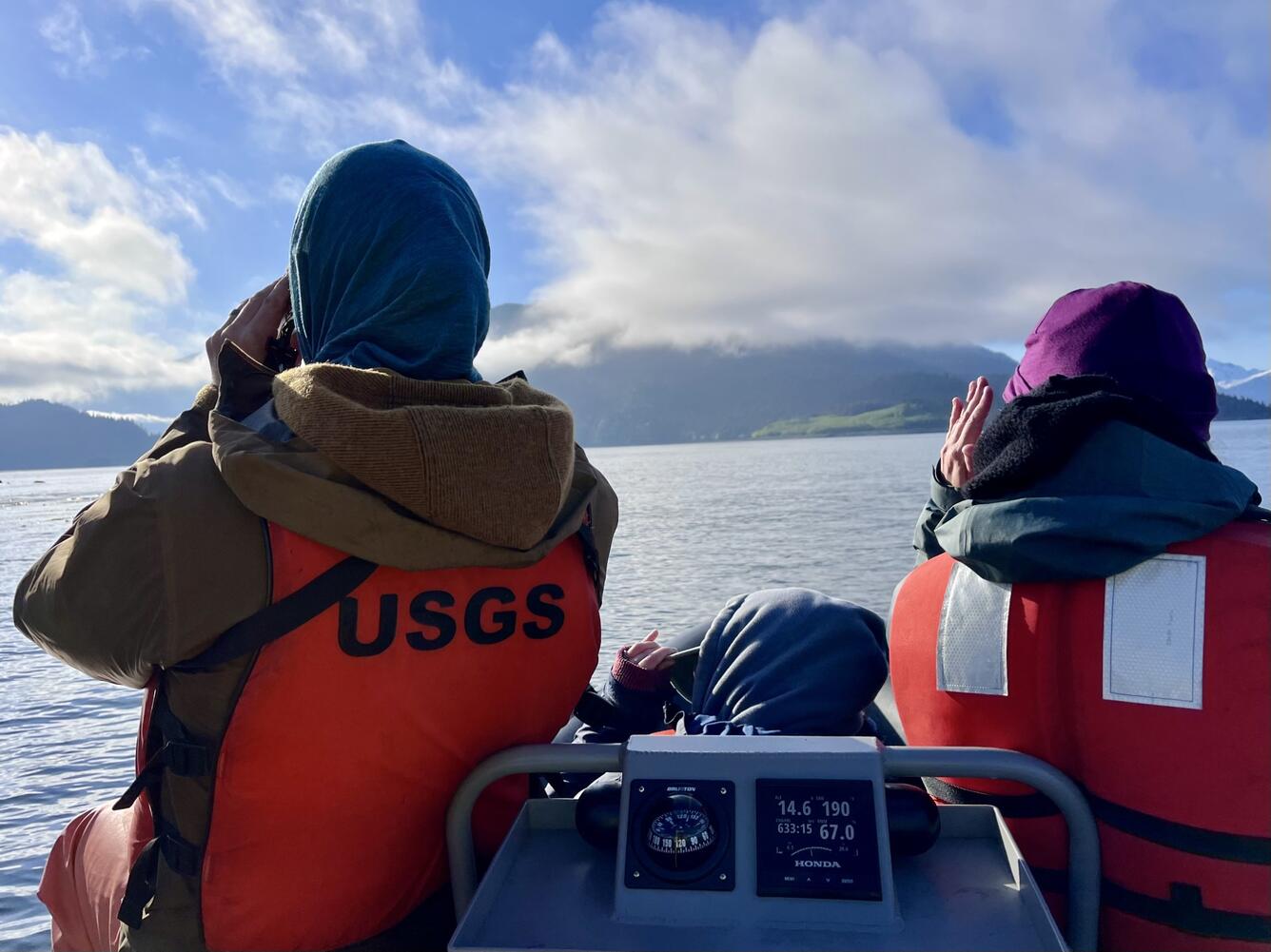 Two people wearing orange life jackets facing away from the camera.