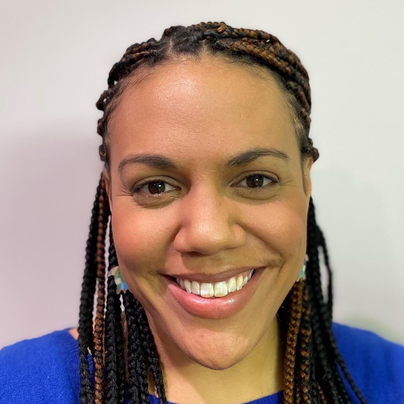 Head shot of a smiling woman with long brown braids wearing a royal blue sweater