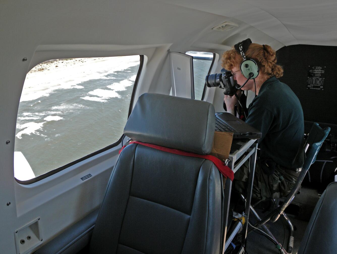 A woman taking photos out the window of an aircraft