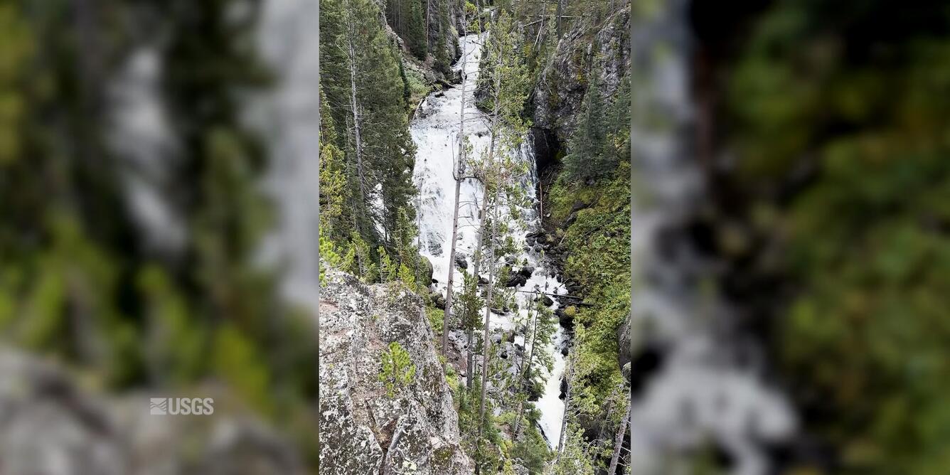A very tall waterfall in the distance behind trees in the foreground.