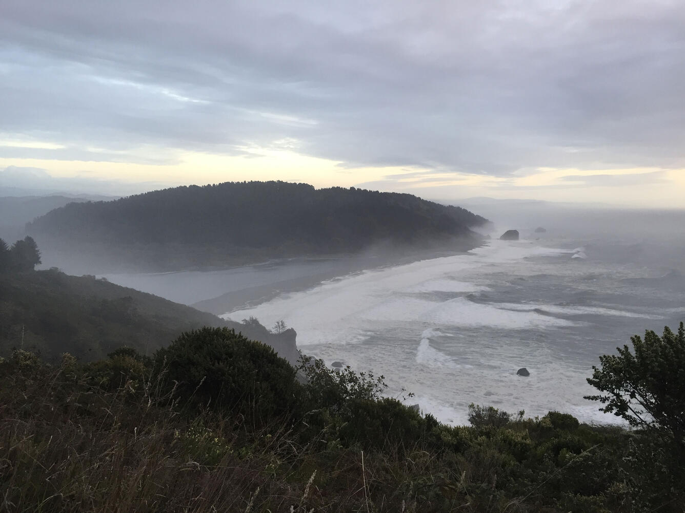 View looks down at the mouth of a river at the ocean from high up on a cliff.
