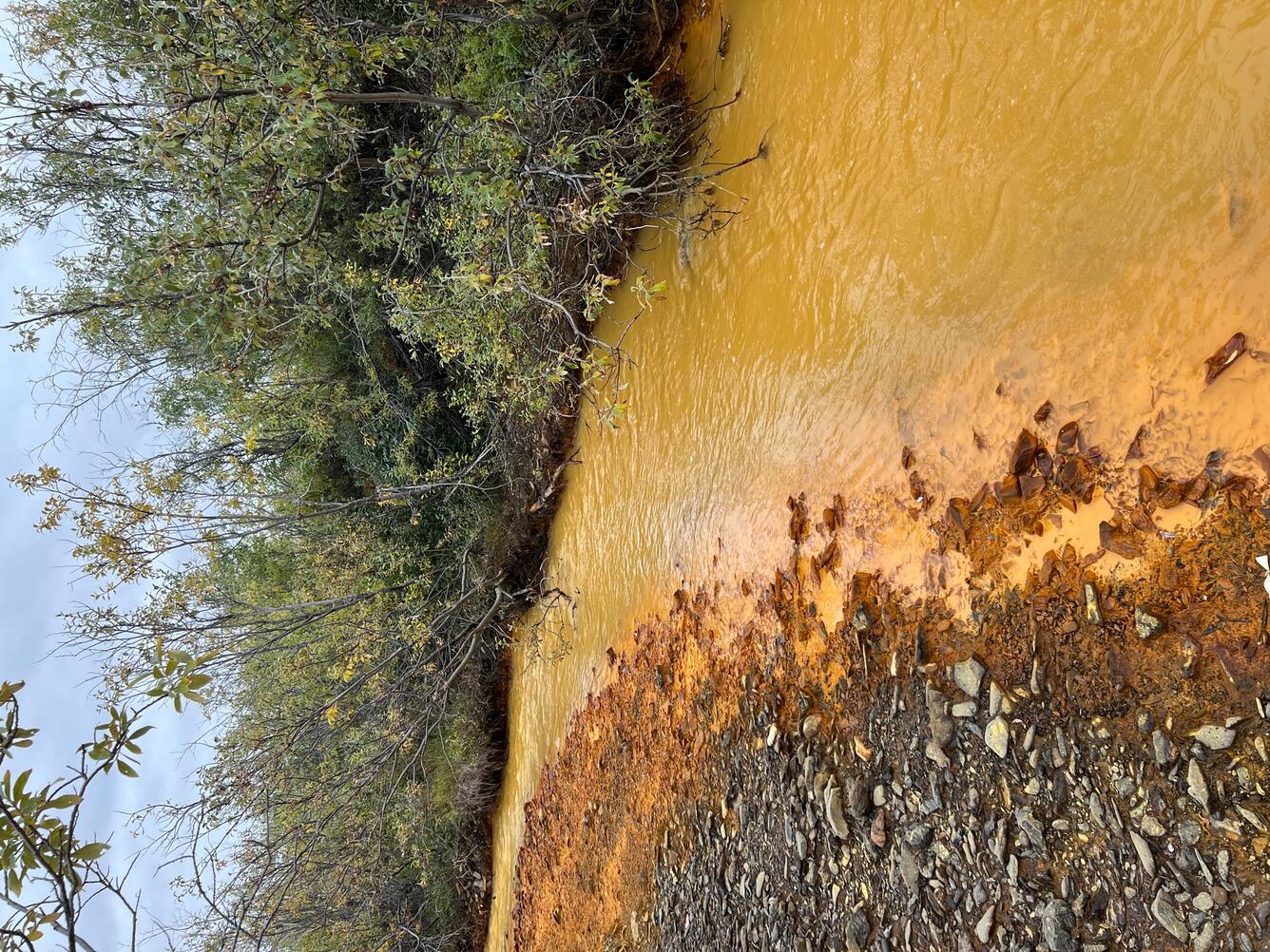 A pale orange river and dark orange deposits on river bank.
