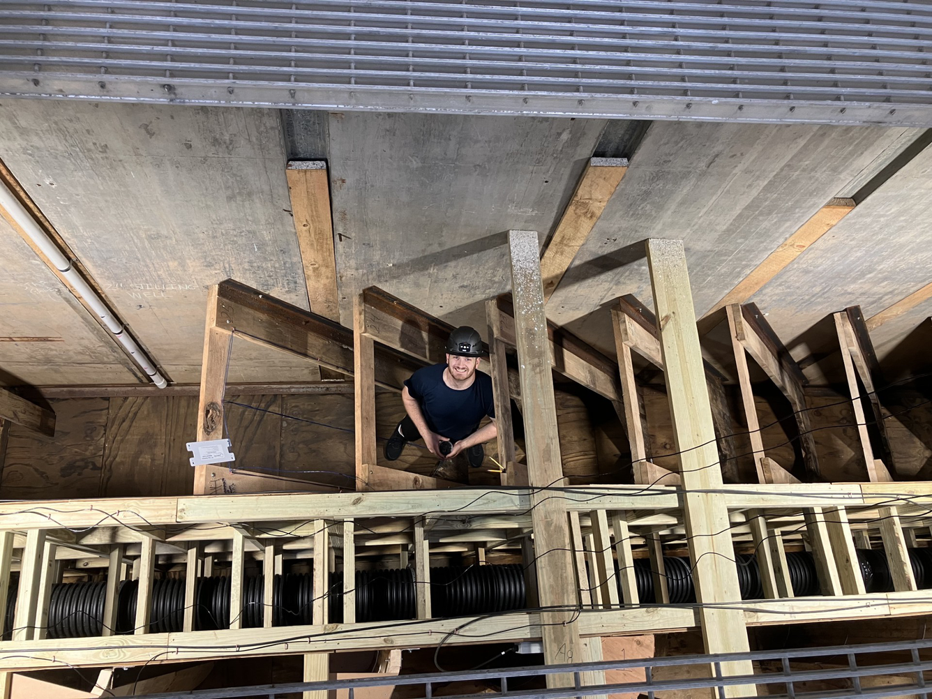 Young man wearing a hard hat stands in the wooden baffles of a de-watered fish ladder
