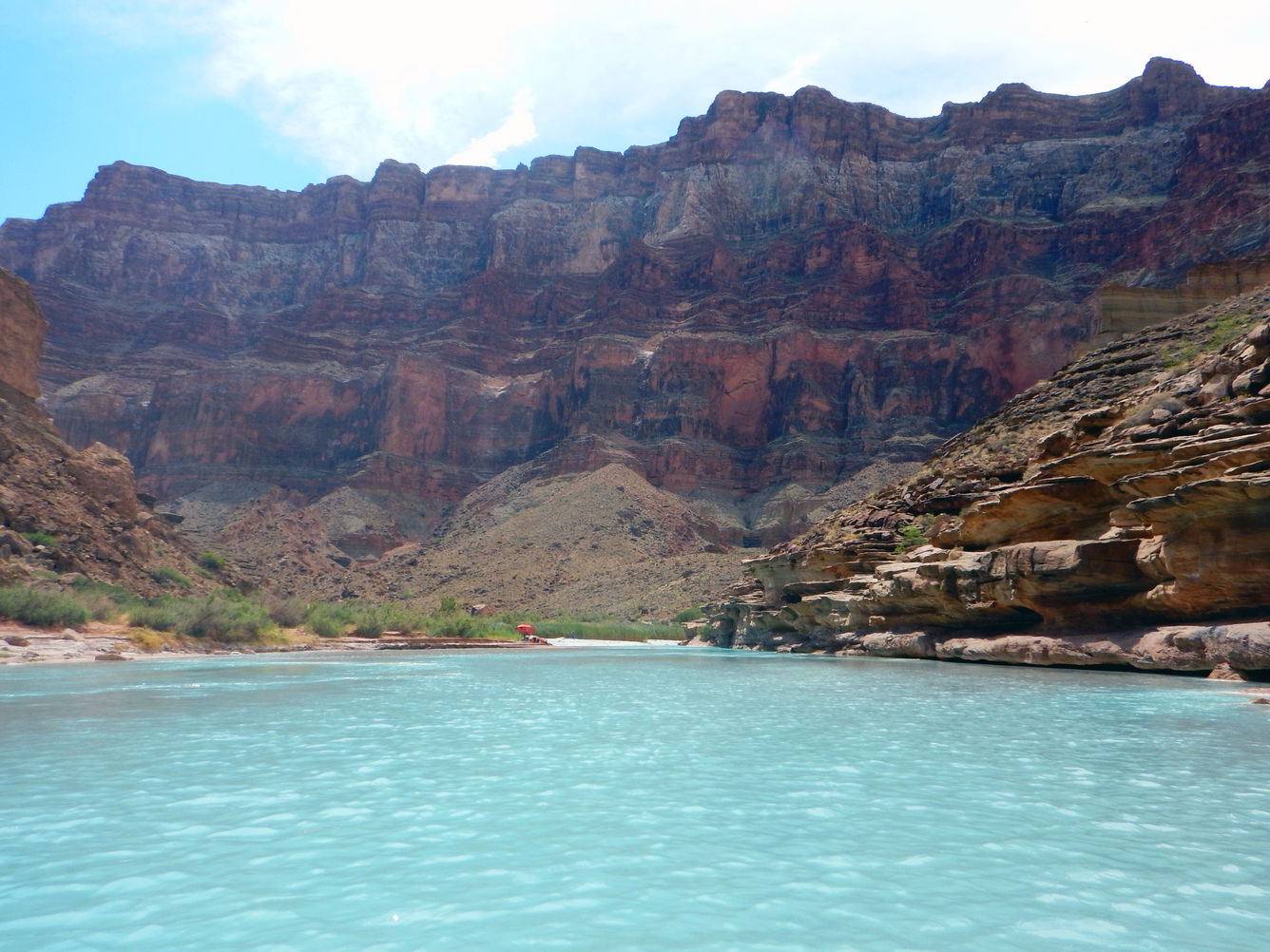 A red shade umbrella in the distance along the light blue Little Colorado River in Grand Canyon