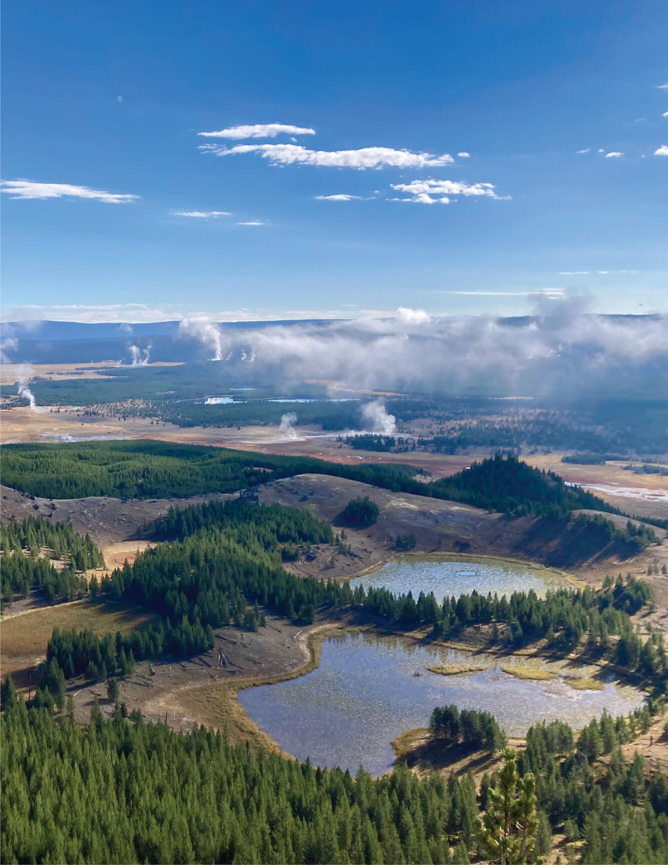Small lakes occupy a landscape of forests and meadows under partly cloudy sky