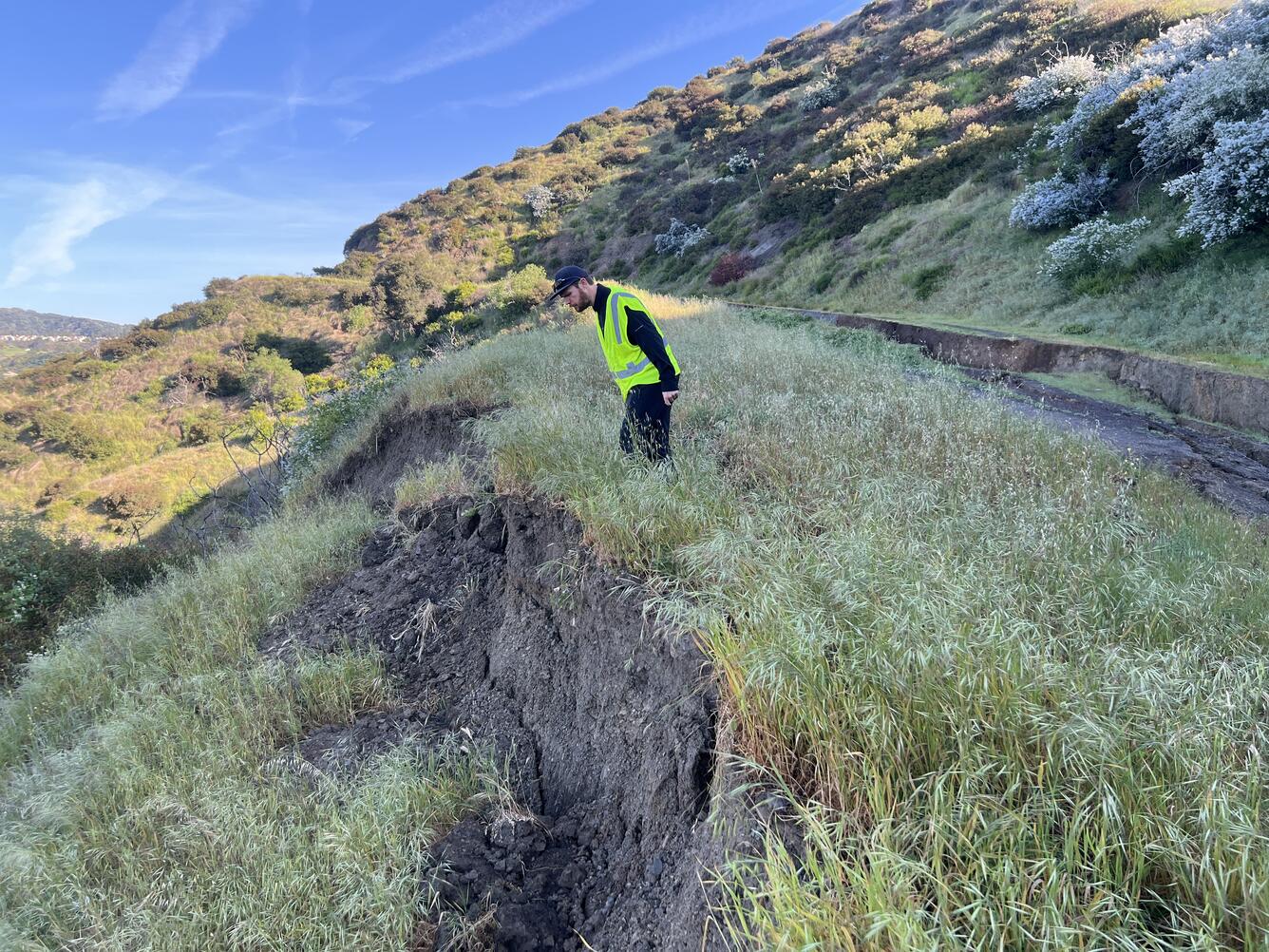 Person standing at top of hillslope looking down at landslide scarp