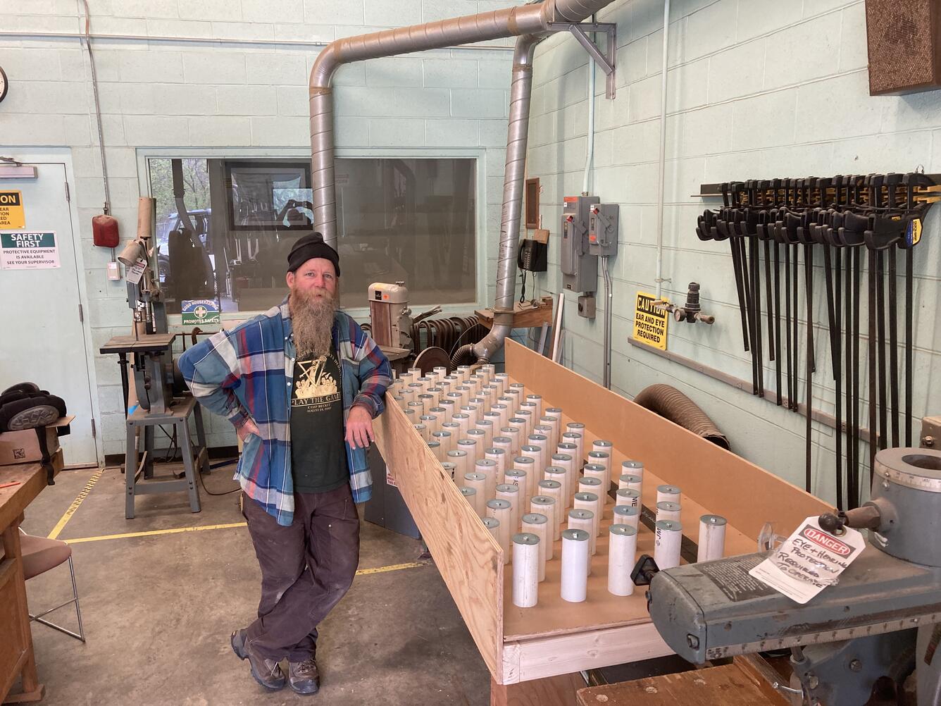Man stands next to an approximately 2.5 ft x 8 ft long wooden ramp with a staggered array of PVC pegs in a workshop.