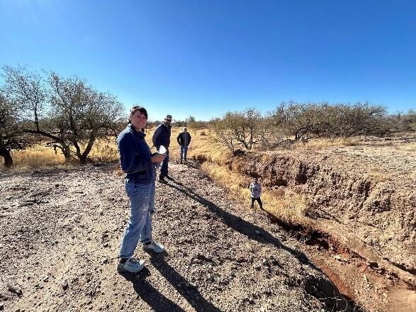 Figure 2. Photographs around the Santa Margarita Ranch including, a) USGS scientists investigating vertical-walled crack from degraded earthen berm; b) vibrant desert landscape featuring a "carpet" of golden Mexican Gold Poppies and purple Coulter's Lupine blooming among rocky soil and sparse vegetation; c) incising narrow, eroded gully or wash cutting through a dry, hilly landscape, and; d) desert arroyo (also known as a dry wash), characterized by a deep, eroded gully carved into the sandy, arid soil, wit