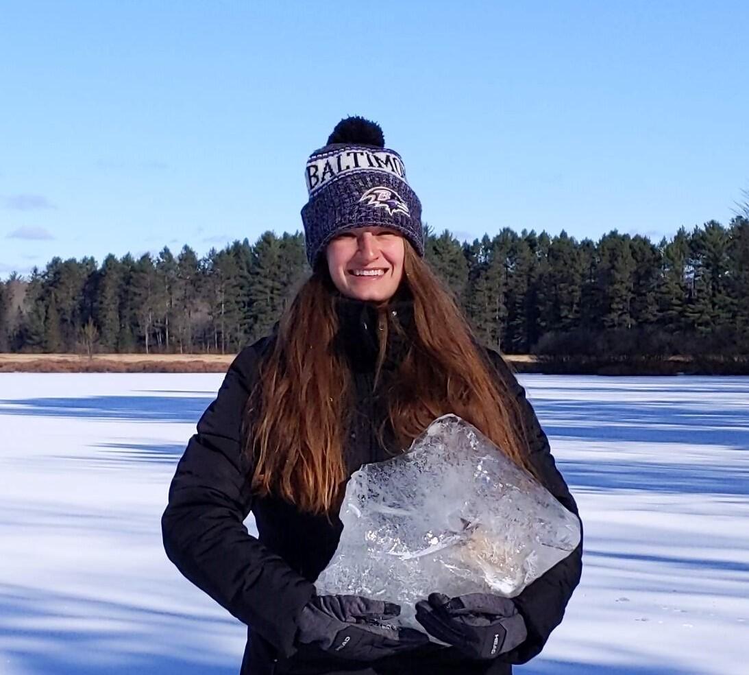 Woman holding large block of ice while standing on frozen lake.