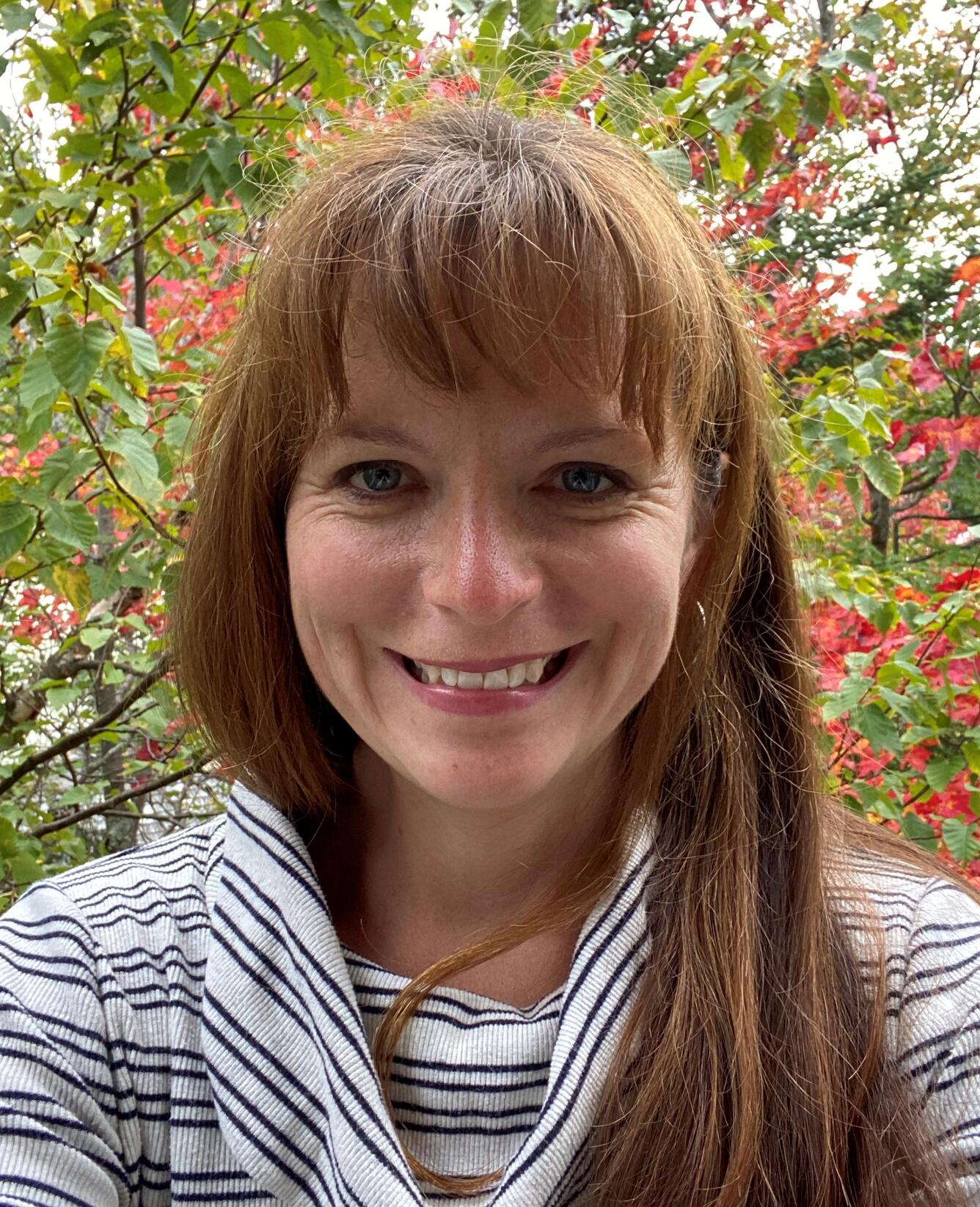 head shot of a smiling woman with flowering shrubbery in the background