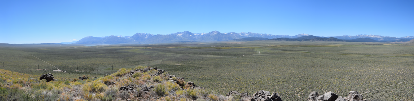 View of a huge valley and distant mountain range. The valley is covered with sagebrush and rock outcrops